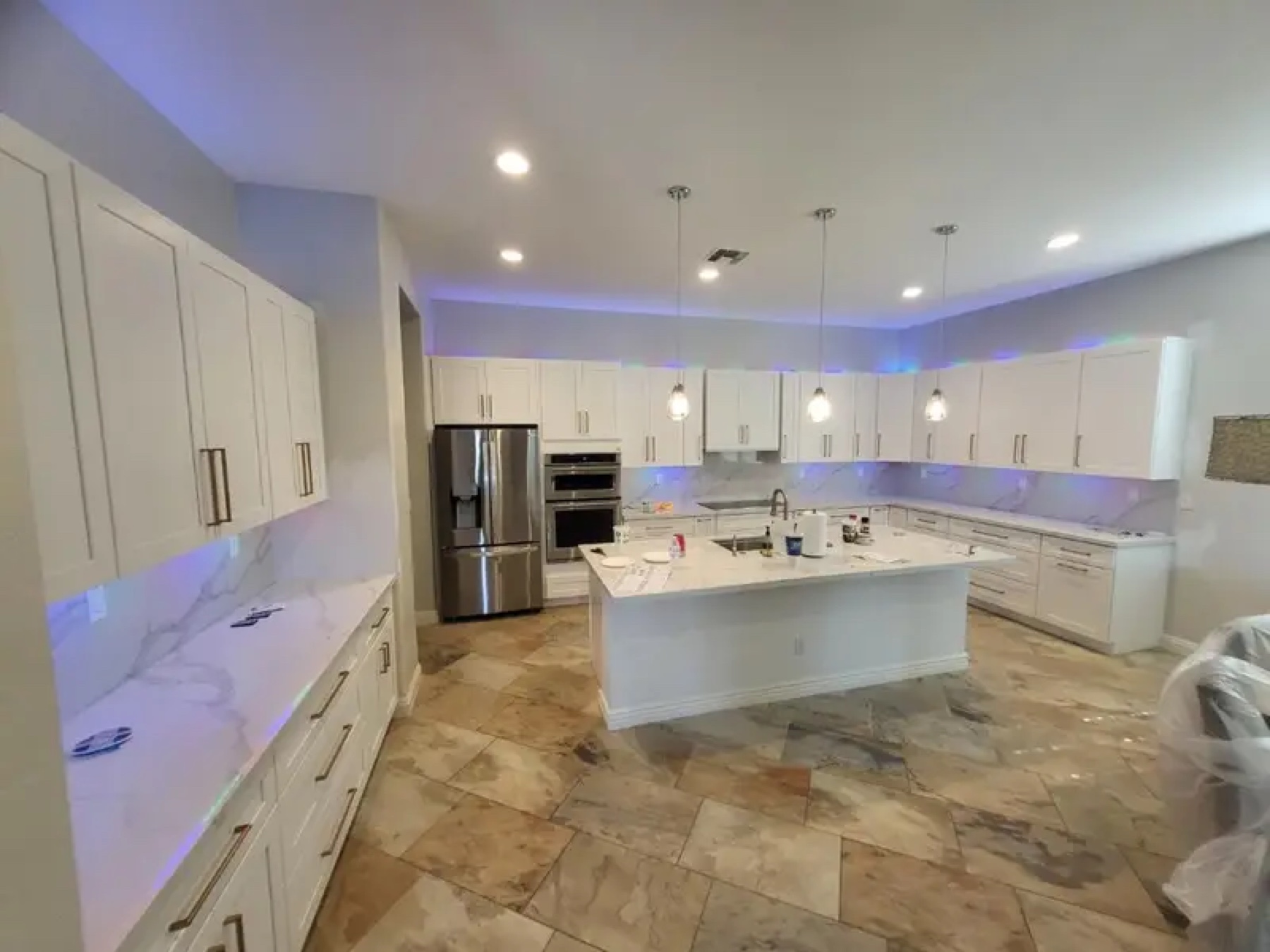 Large white kitchen with marble island and LED pendant lights